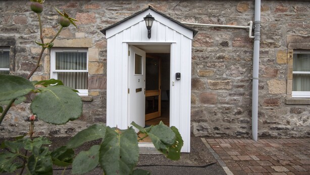 A stone building with a white door and a small window. - 2 Varis Apartments (Forres)
