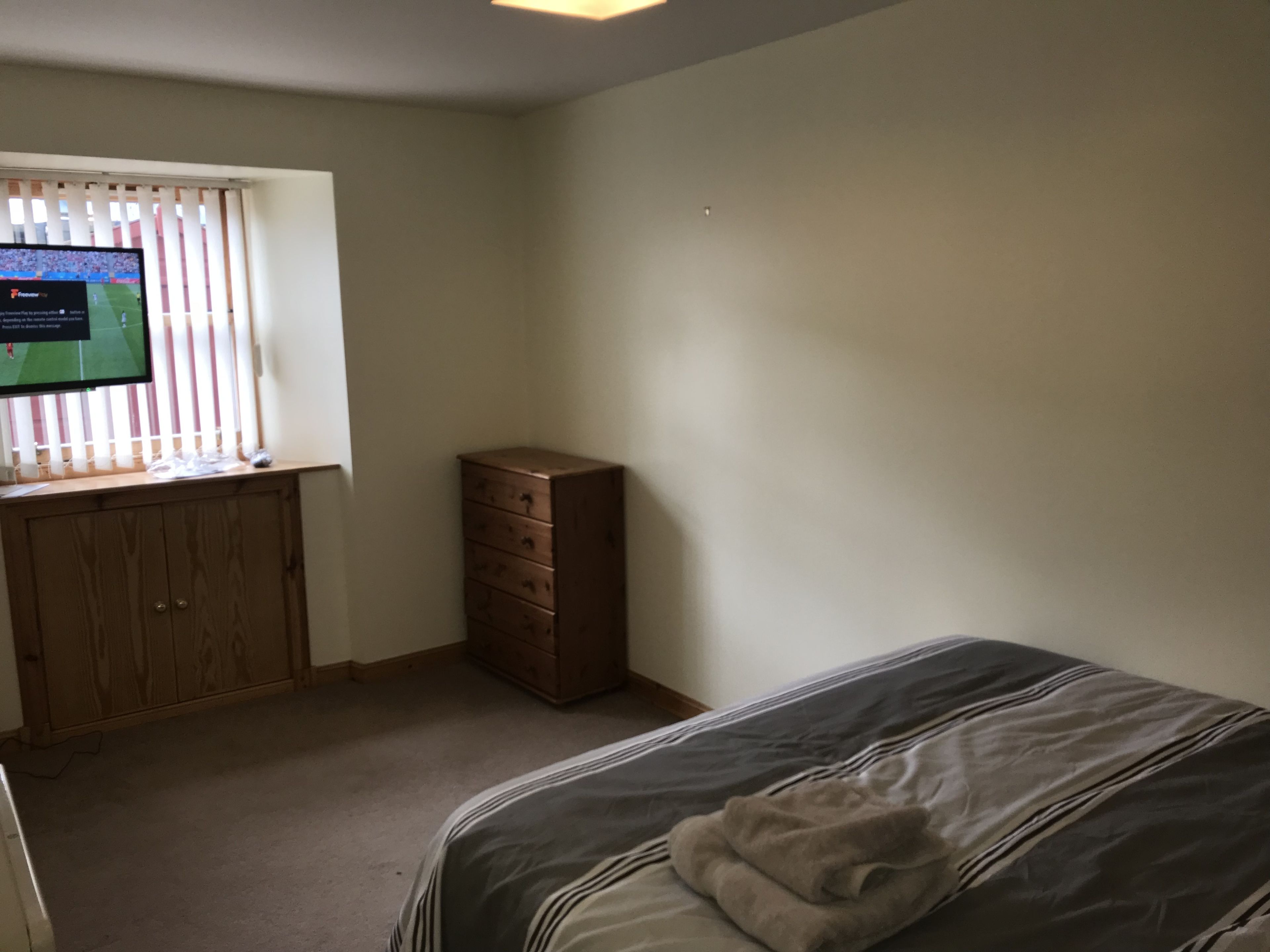 Une chambre à coucher avec un lit, une commode en bois et un téléviseur posé sur un bureau.