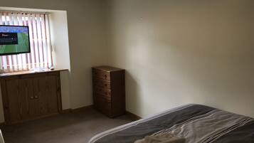 Une chambre à coucher avec un lit, une commode en bois et un téléviseur posé sur un bureau.