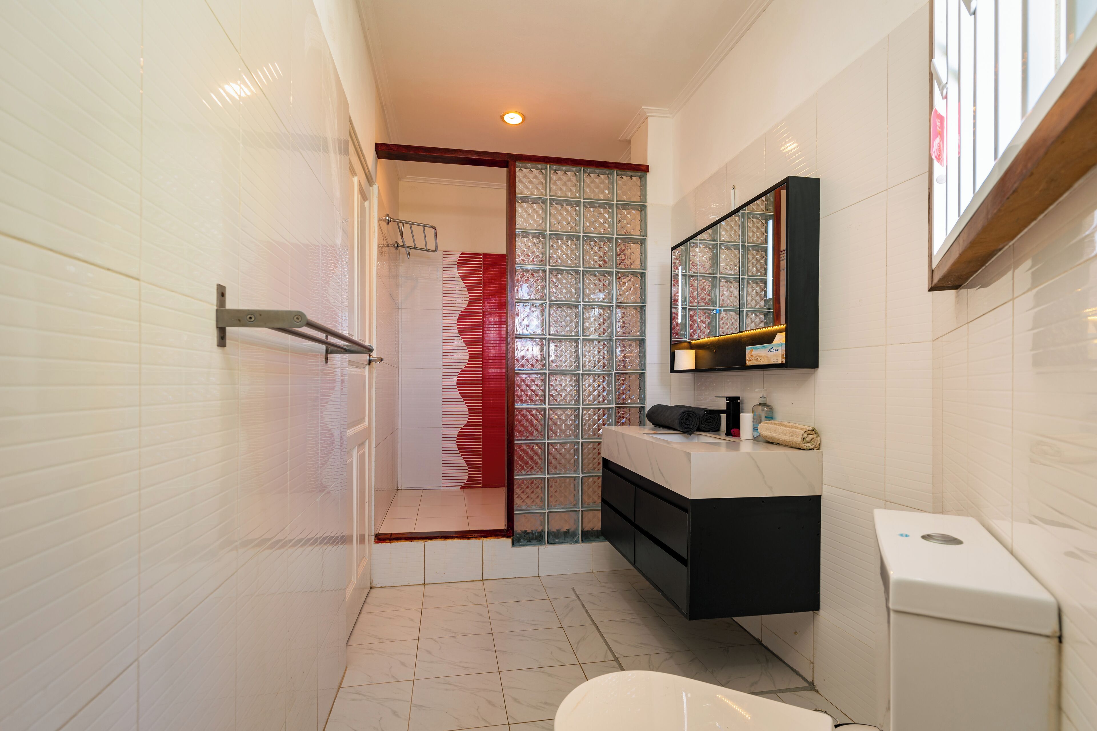 Un baño moderno con inodoro blanco, cabina de ducha de vidrio, tocador negro y espejo sobre el lavabo.