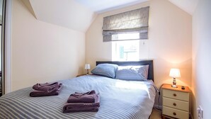 A neatly made bed with striped bedding, a bedside lamp, and a nightstand with a remote control.