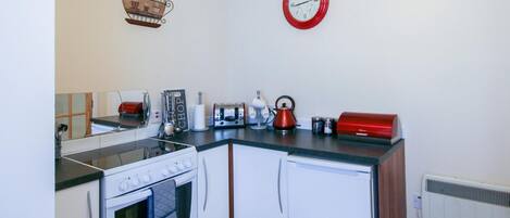 A compact kitchen with a stove, oven, and a red clock on the wall.