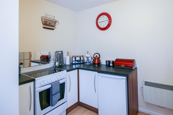 A compact kitchen with a stove, oven, and a red clock on the wall. - 7 Varis Apartments (Forres)