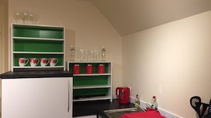 A kitchen with white cabinets, green shelves, and a red kettle.