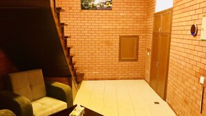 Une petite pièce fermée, avec un mur en briques, une armoire en bois, un canapé, une table basse et un escalier.