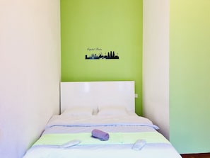 A bed with a green wall behind it, a pillow, a rolled towel, and a blanket.
