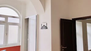 Une pièce dotée d’une grande fenêtre en arc de cercle, d’une porte avec un miroir et d’une enseigne fixée au mur représentant une mosquée.