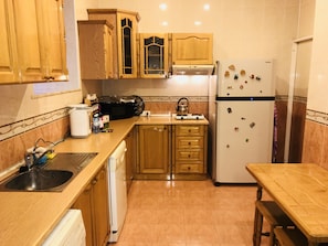 A compact kitchen with wooden cabinets, a built-in microwave, a refrigerator, and a small dining table.