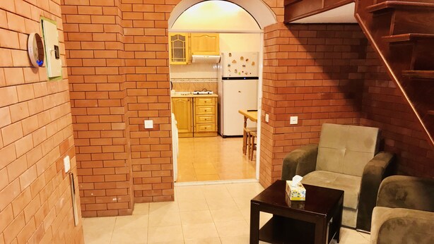Un salon avec un mur en briques, un escalier en bois et une cuisine à l’arrière-plan.