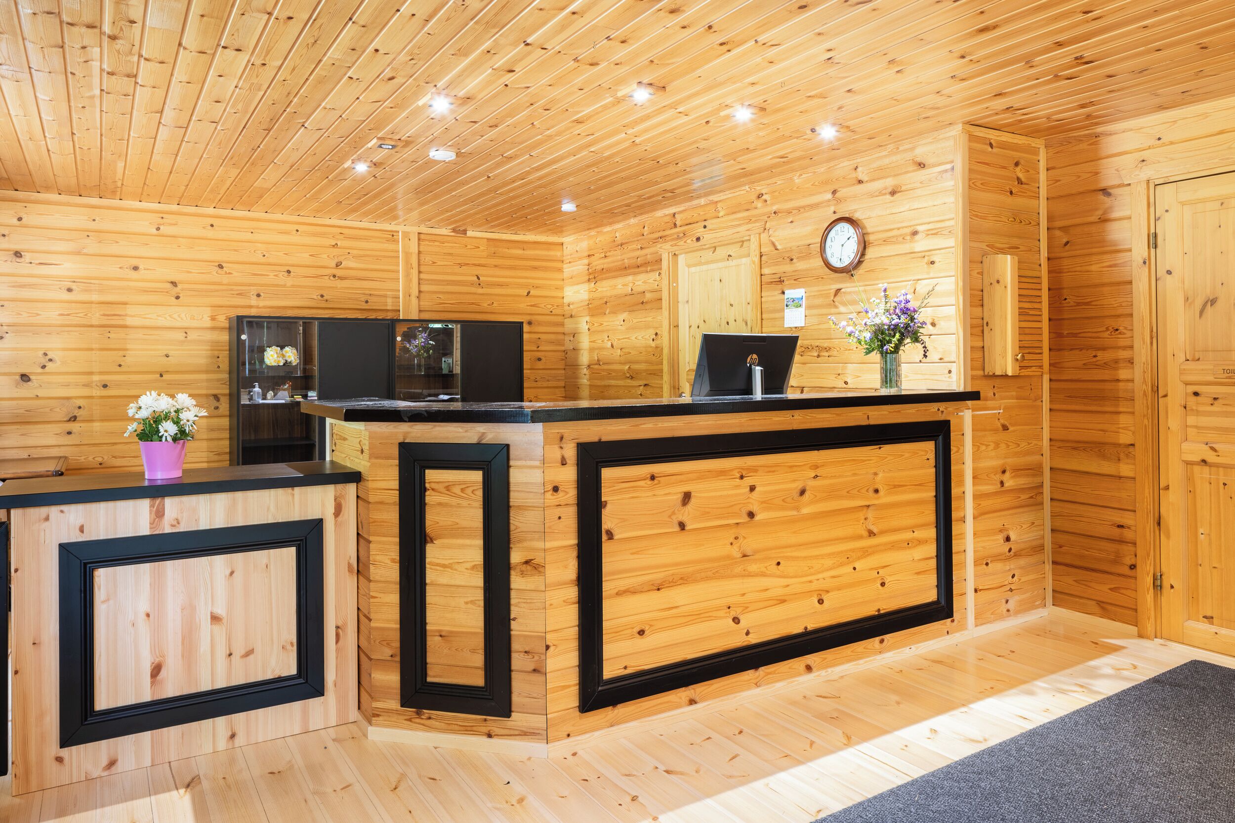 Un intérieur en bois comprenant un comptoir d’accueil, une horloge et un petit arrangement floral.