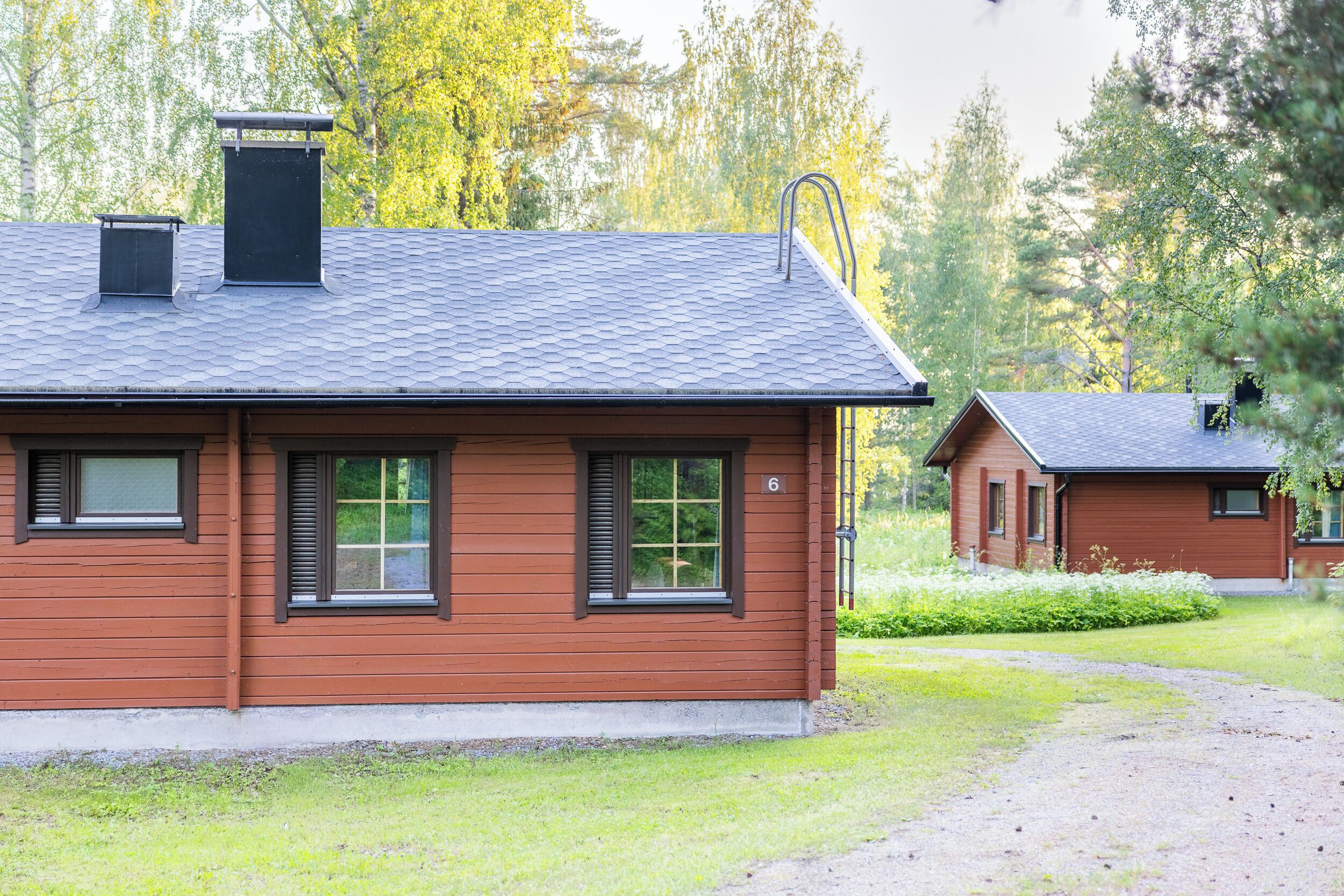 Puinen mökki, jossa on kalteva katto, savupiippu ja pieni erillinen varasto.