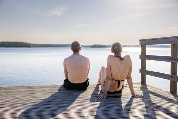 Two people sitting on a wooden dock overlooking a calm body of water. - Hapimag Resort Punkaharju (Savonlinna)