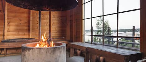 A rustic interior with a large fireplace, wooden benches, and a view through a window.