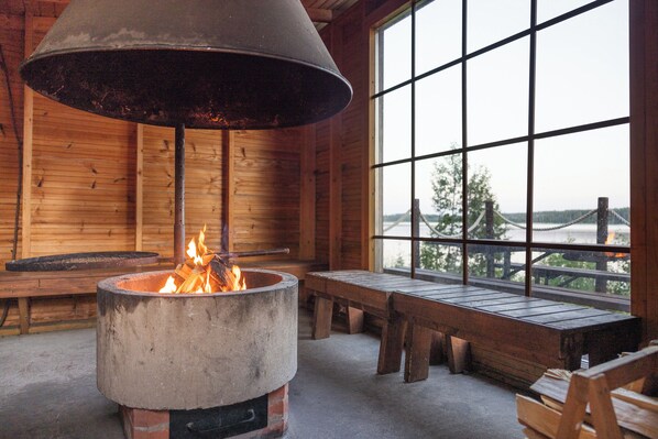 A rustic interior with a large fireplace, wooden benches, and a view through a window. - Hapimag Resort Punkaharju (Savonlinna)