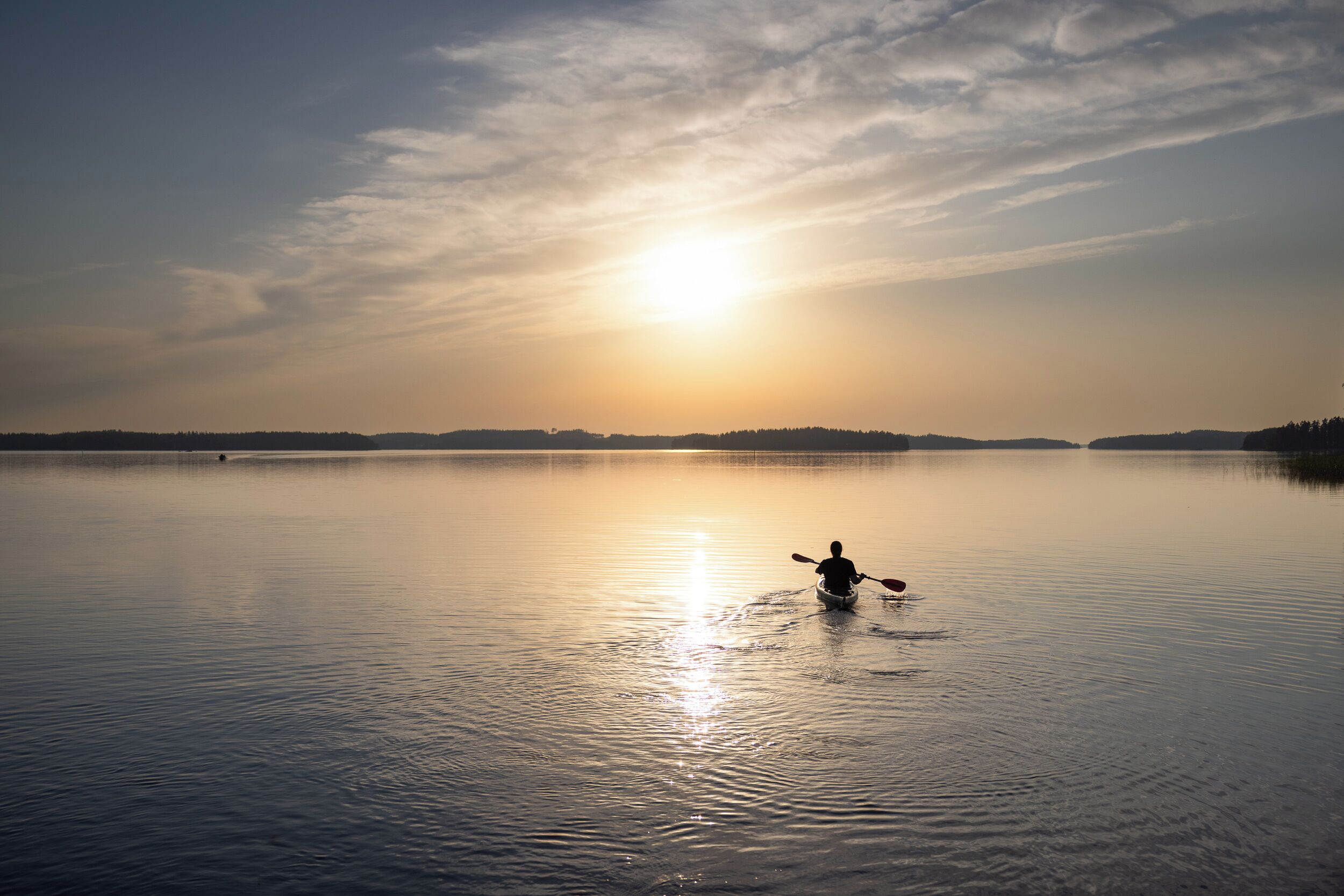 En rolig sø med en person i kajak, omgivet af et skovlandskab og en klar himmel.