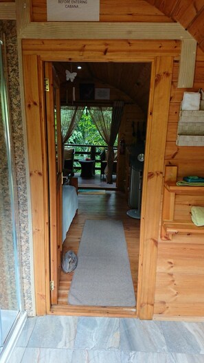 Entrada a una cabaña de madera con una cama, una alfombra pequeña y suelo de baldosas de piedra.