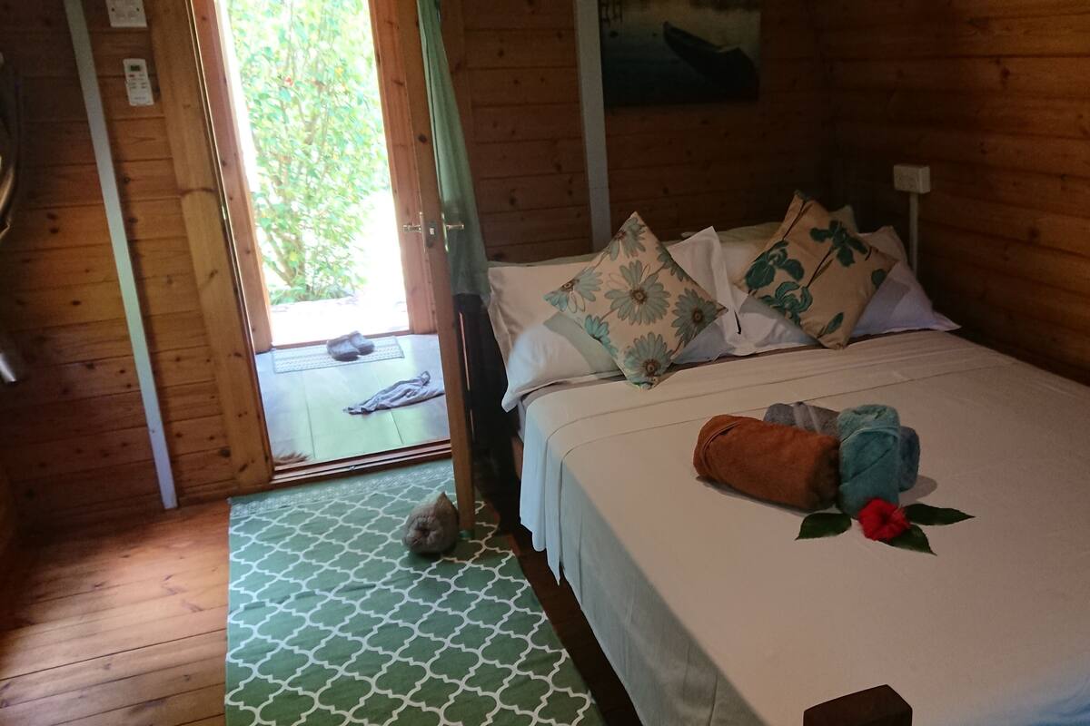 A wooden cabin room with a bed, pillows, and a blanket.
