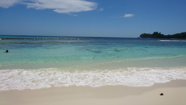 Una playa con aguas turquesas cristalinas, arena blanca y una isla distante.
