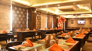 A restaurant with multiple tables set with orange napkins, glasses, and cutlery. - The Grand Empire A Boutique Hotel (Patna)