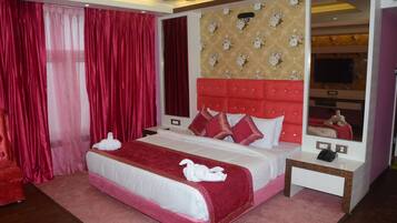 A hotel room with a large bed, red curtains, a red headboard, and a mirror.