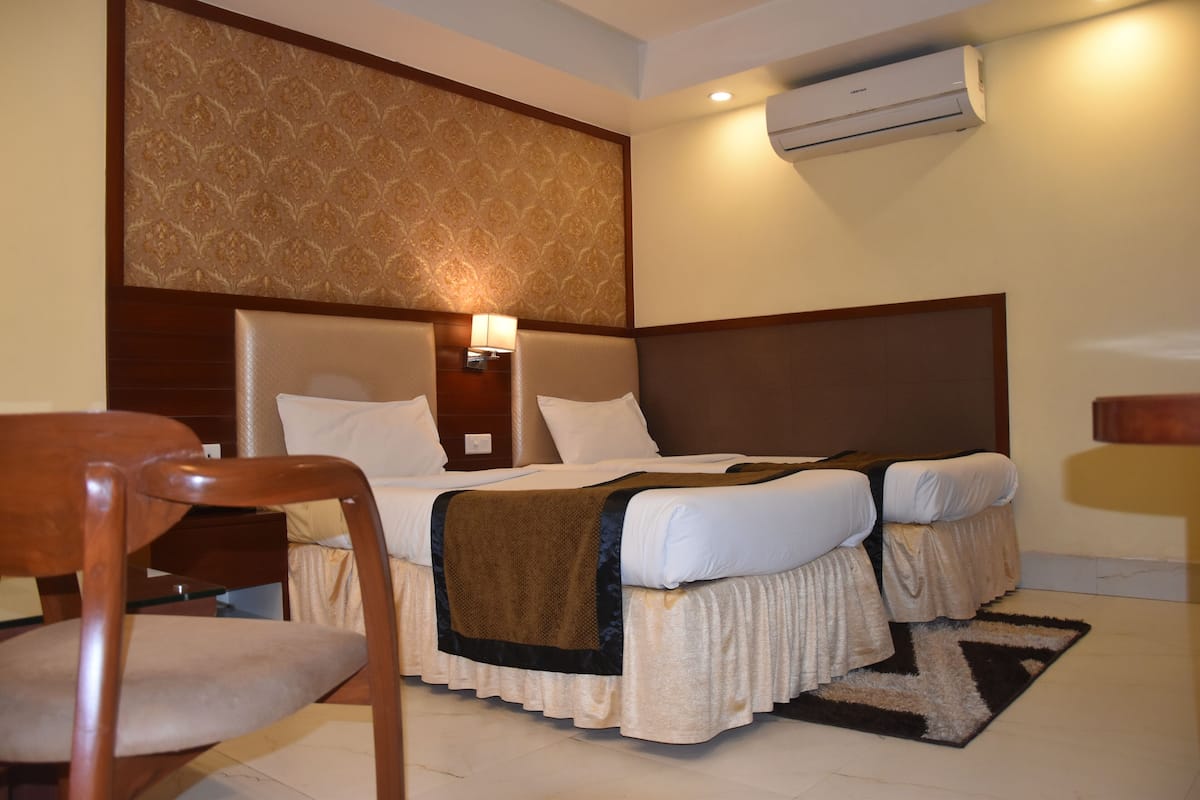 Une chambre d’hôtel avec un grand lit, deux tables de chevet, une chaise, un appareil de climatisation et un mur décoré d’un motif.