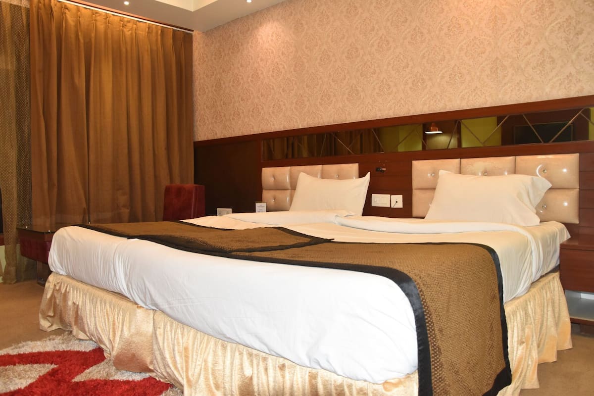 Un grand lit avec une tête de lit, une chaise rouge et un mur orné d’un motif.