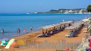 A beach with tents, umbrellas, and lounge chairs. - Alekos Beach Houses-Infinity (Kefalonia)