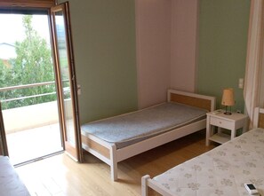 A small bedroom with a single bed, a nightstand with a lamp, and a sliding glass door leading to a balcony.