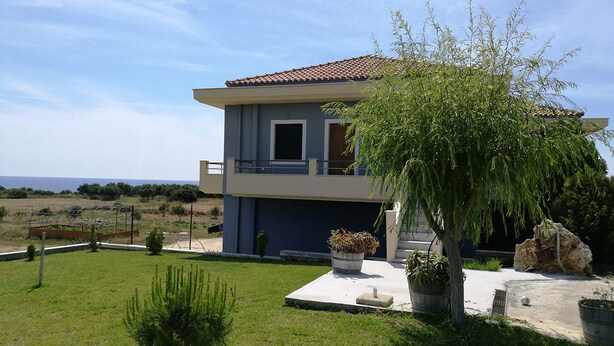 A two-story house with a balcony, a garden with a small tree, and a view of the sea. - Alekos Beach Houses-Angelo (Kefalonia)