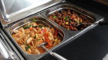 Un buffet con due vassoi metallici pieni di verdure saltate e carne.