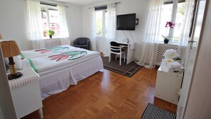 Habitación de hotel con cama, escritorio, silla, televisor y un baño pequeño.
