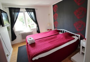 Un dormitorio con cama, radiador, televisor y ventana con cortinas.