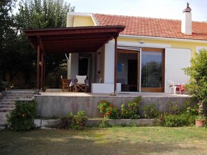 A house with a covered patio, a sliding glass door, and a small garden area with steps leading to the entrance. - Alekos Beach Houses-Nisos (Kefalonia)