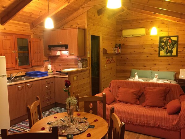Un acogedor interior de cabaña con paredes de madera, una zona de comedor con mesa y sillas, una kitchenette y un sofá rojo.