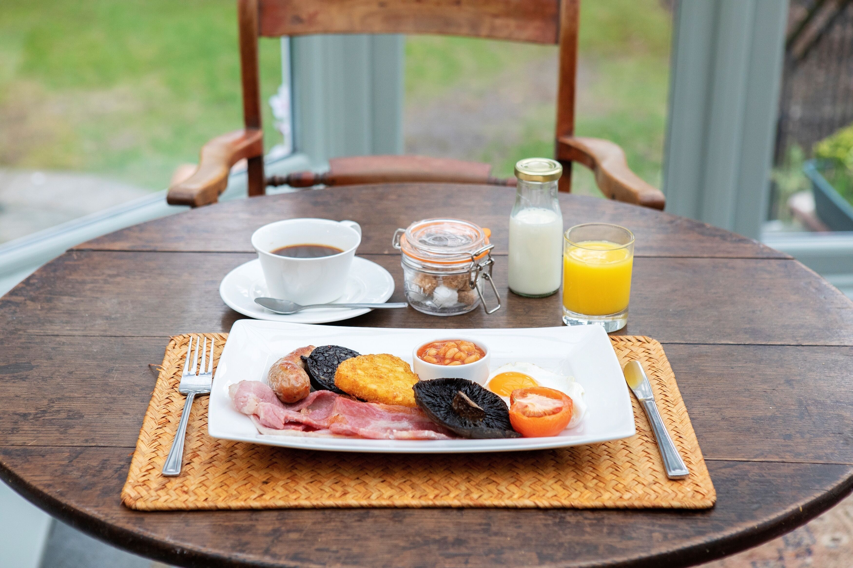 Un desayuno con un plato de comida, un vaso de zumo de naranja, una botella de leche y una taza de café sobre una mesa de madera.