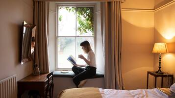 A room with a bed, a desk, a chair, a window with curtains, and a lamp.
