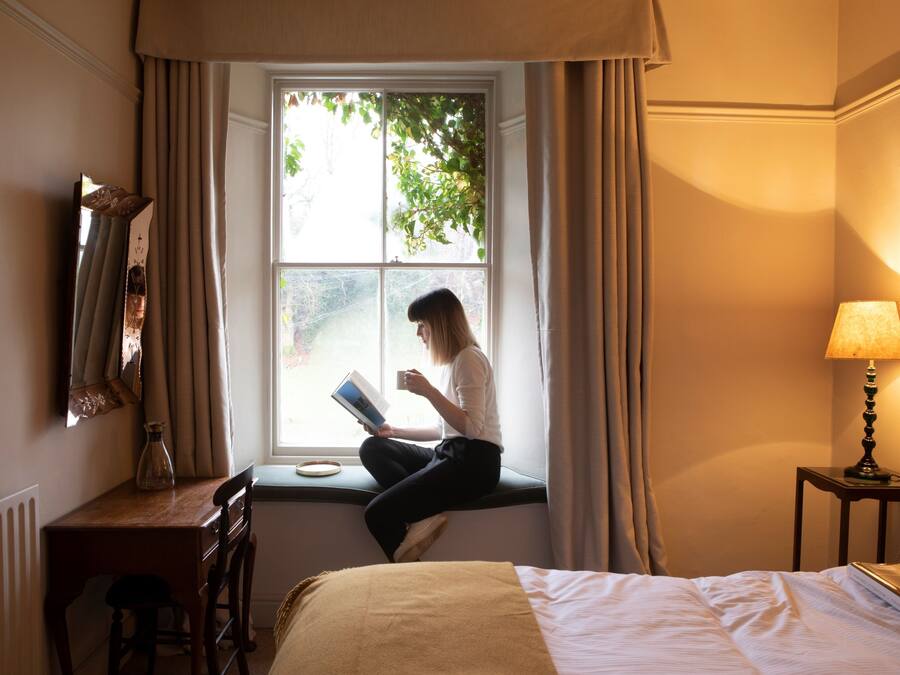 A room with a bed, a desk, a chair, a window with curtains, and a lamp.