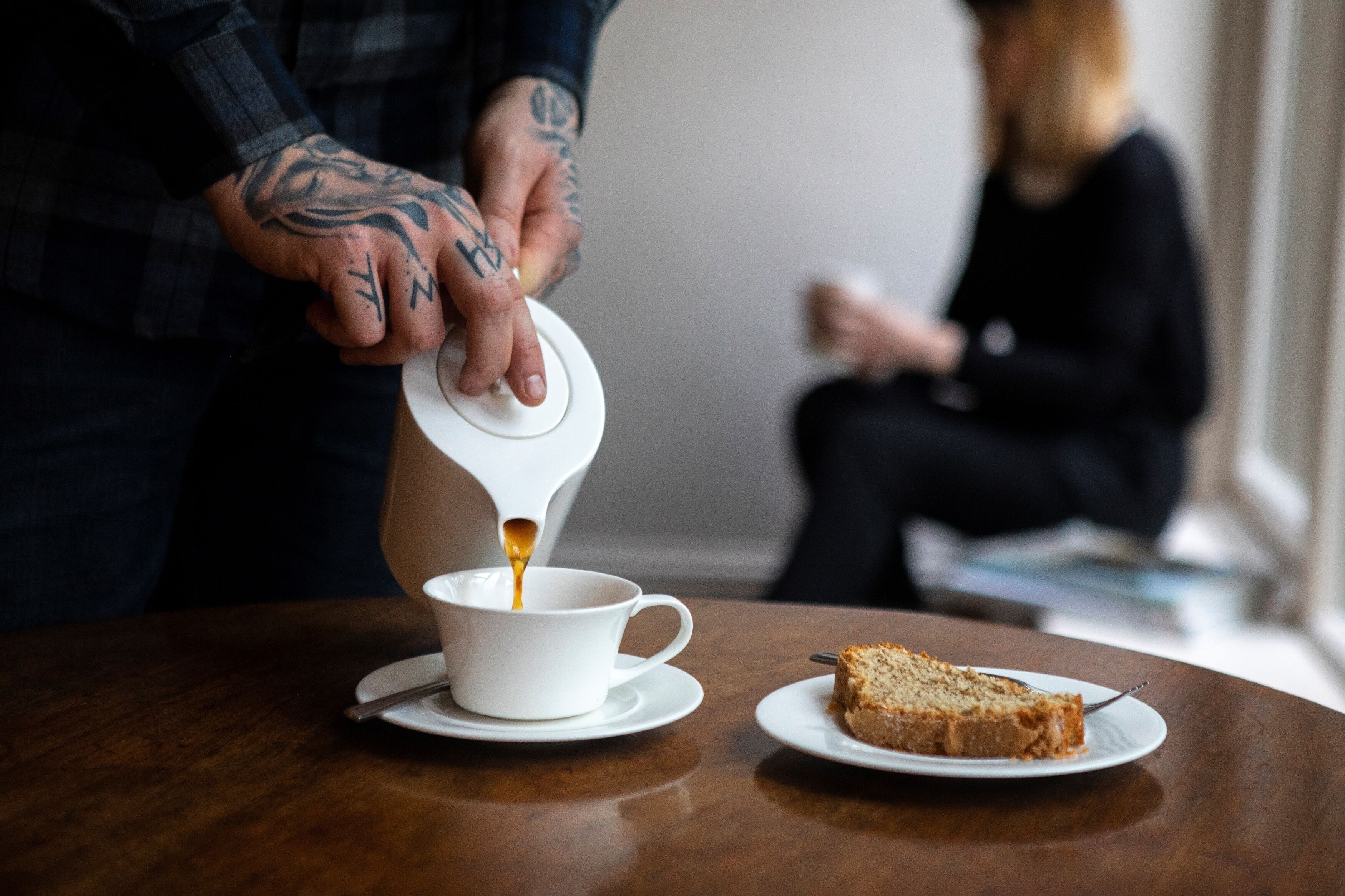 Une personne verse du café dans une tasse posée sur une table, à côté d’une part de gâteau.