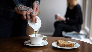 Jemand schenkt Kaffee in eine Tasse auf einem Tisch ein, daneben liegt ein Stück Kuchen.