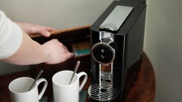 Una cafetera con pantalla digital, dos tazas blancas sobre un posavasos y una cuchara dentro de una taza.