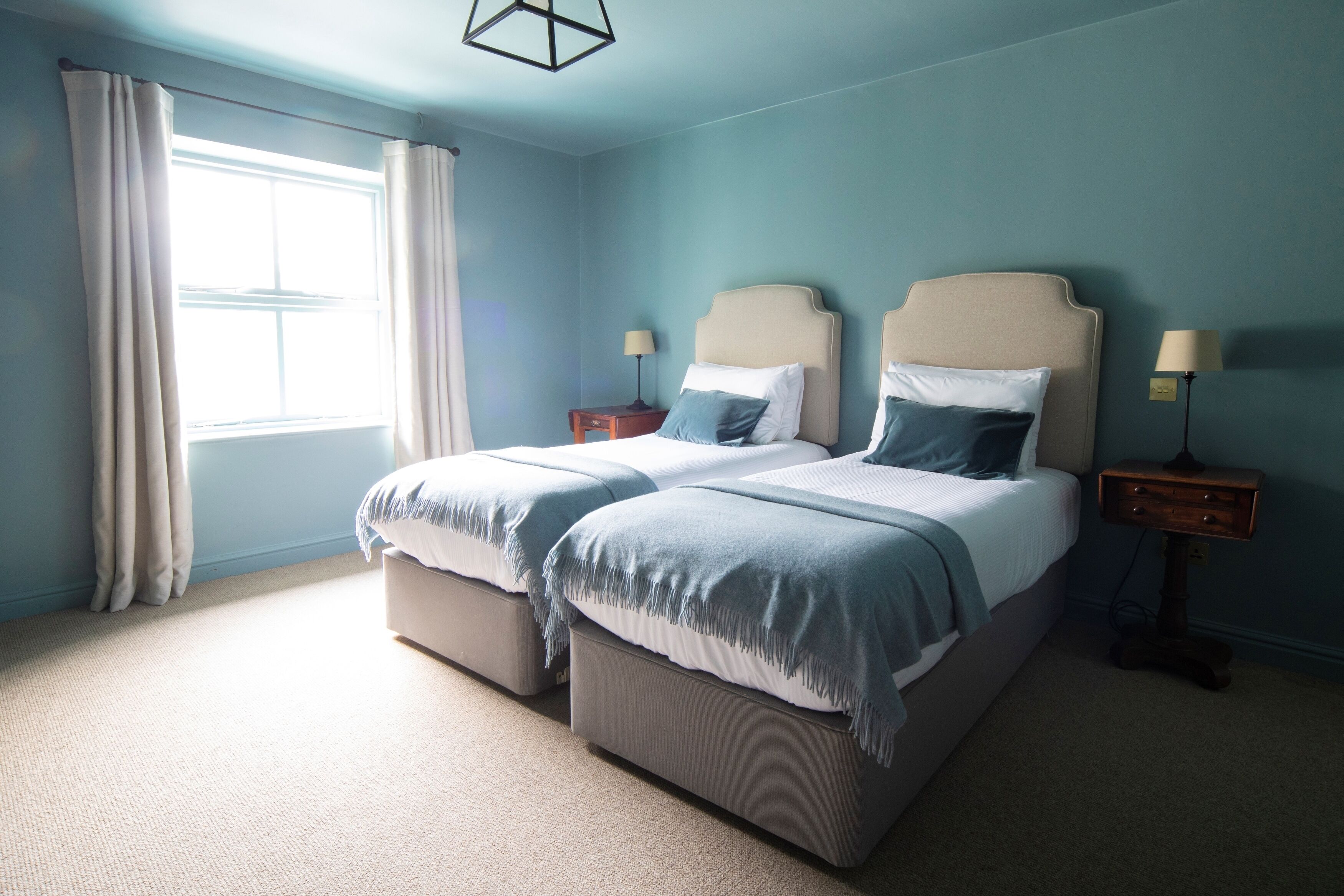 A double bed with a headboard, two bedside tables, a lamp, and a window with curtains.