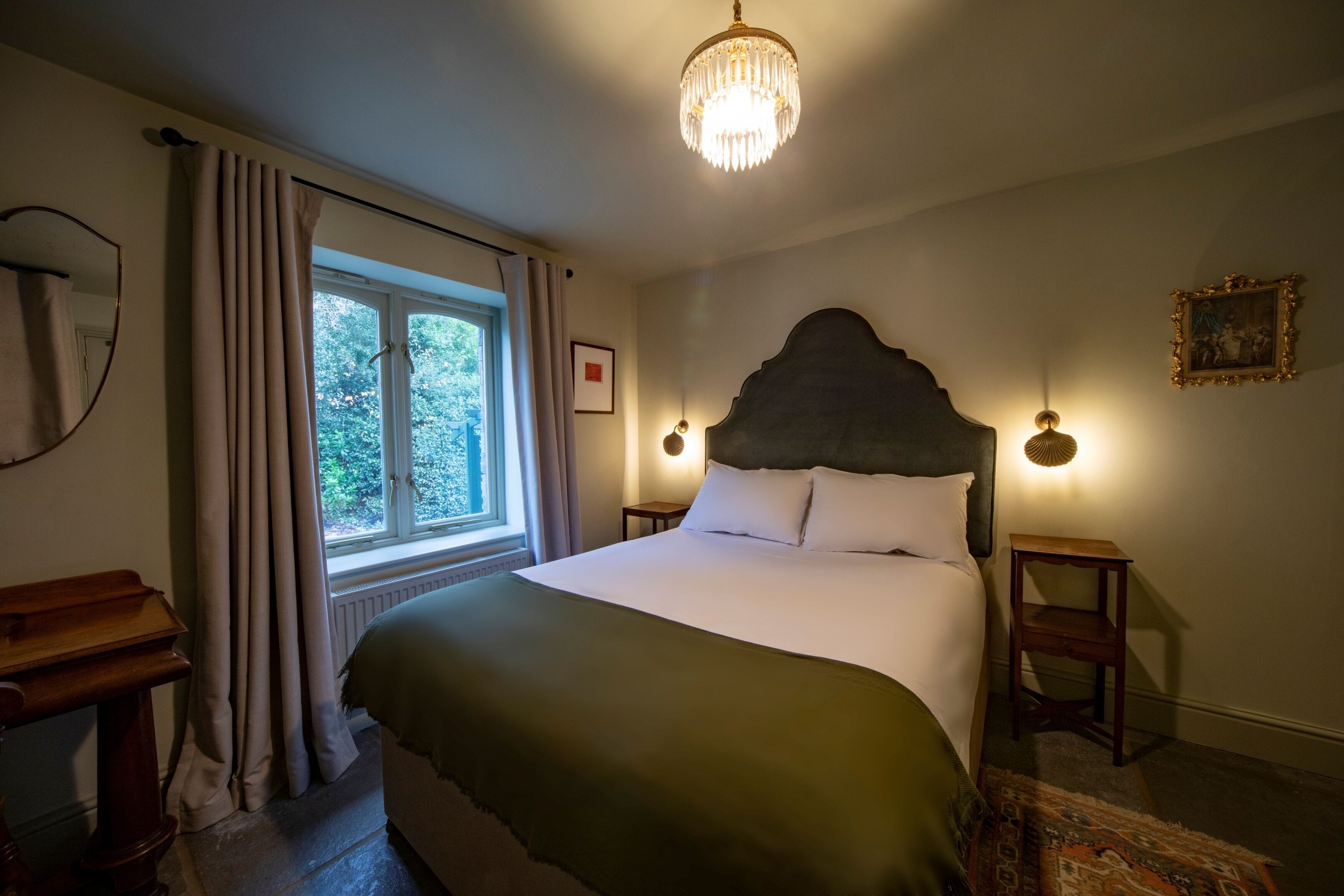 A bedroom with a large bed, a window with curtains, a chandelier, and a framed picture on the wall.