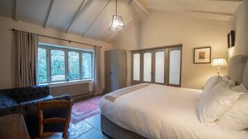 A bedroom with a large bed, a wooden chair, a window with curtains, and a hanging light fixture.