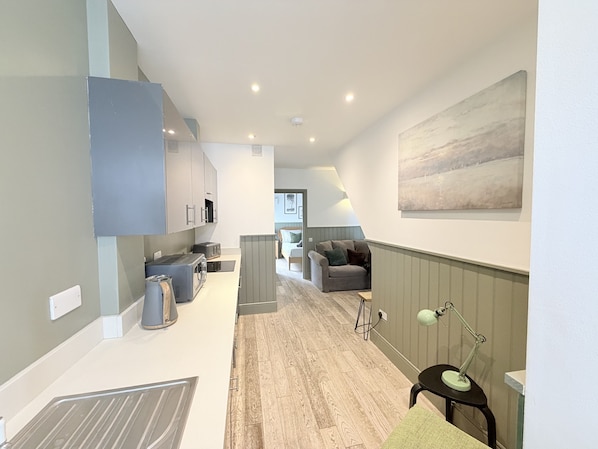 A modern kitchen with built-in appliances, a dining area with a table and chairs, and a living room with a sofa and a painting on the wall.