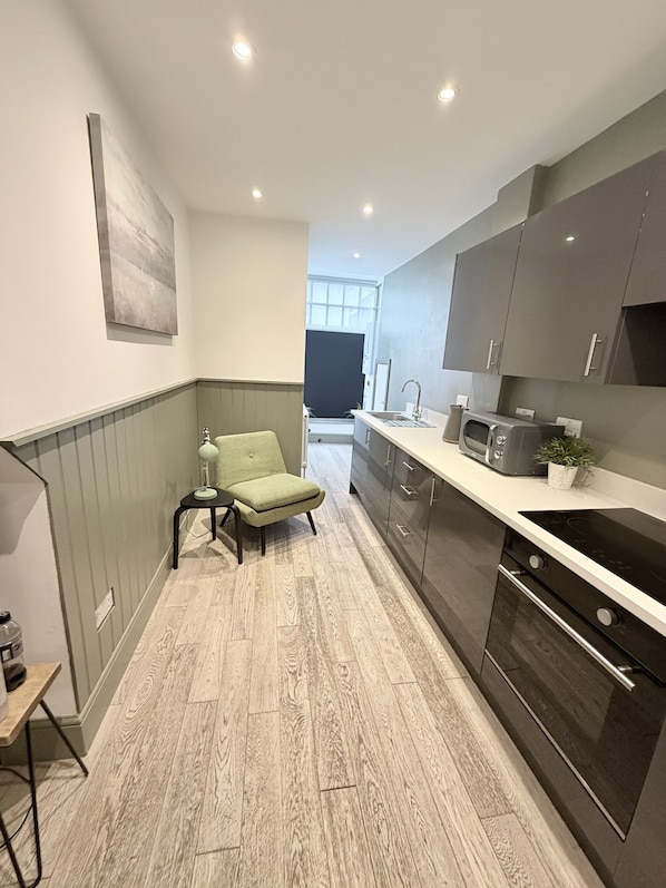 A modern kitchen with grey cabinets, a black countertop, a microwave, and a small plant. - The Urban Retreat (Southampton)