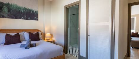 A bedroom with a bed, a nightstand, a lamp, a glass door leading to a shower, and a painting on the wall.