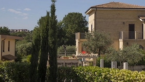 A two-story building with a tiled roof, a balcony, and a garden area with shrubs and trees. - B&B Villa Saraceni (Vasto)