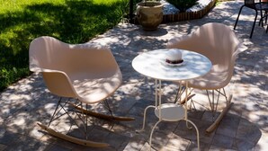 A patio with two rocking chairs and a small round table, surrounded by a stone pathway and greenery. - B&B Villa Saraceni (Vasto)