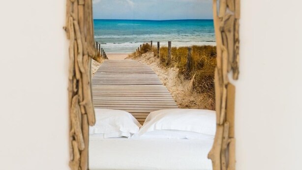 A bedroom with a wooden bed, white bedding, and a view of a beach through a rustic mirror frame. - B&B Villa Saraceni (Vasto)