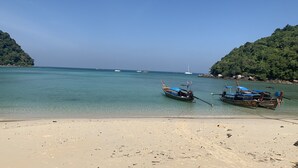 Une plage où deux bateaux sont amarrés près du rivage, entourée de collines verdoyantes.